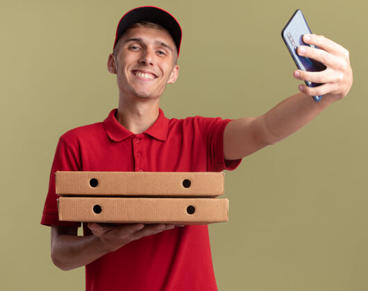 男孩带着微笑的金发送货员拿着比萨饼盒和电话金发披萨盒子