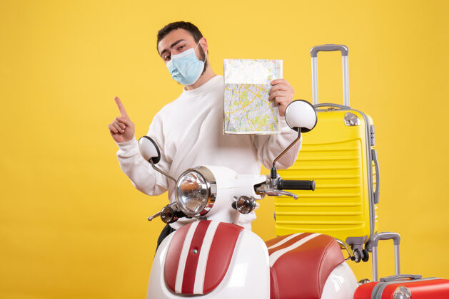 立场旅行概念的俯视图 戴着医用面罩的自信的家伙站在摩托车旁边 黄色手提箱在上面 拿着地图朝上人车辆摩托车