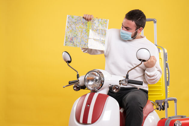 面具旅行的概念与自信的家伙在医疗面具坐在摩托车上 黄色手提箱上 并显示黄色地图人旅行摩托车