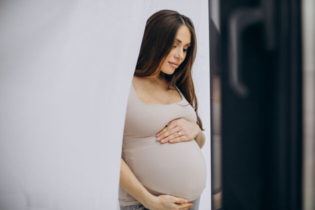 怀孕孕妇抱着肚子站在窗边孩子腹部女性