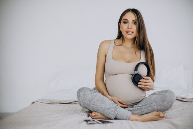 等待孕妇带着超声波照片把带音乐的耳机放在肚子上产前为人父母孩子