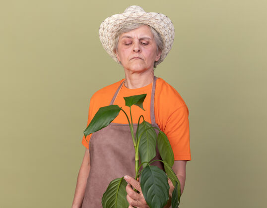 手套自信的上了年纪的女园丁戴着园艺帽和手套 抱着和看着植物枝帽子园艺穿