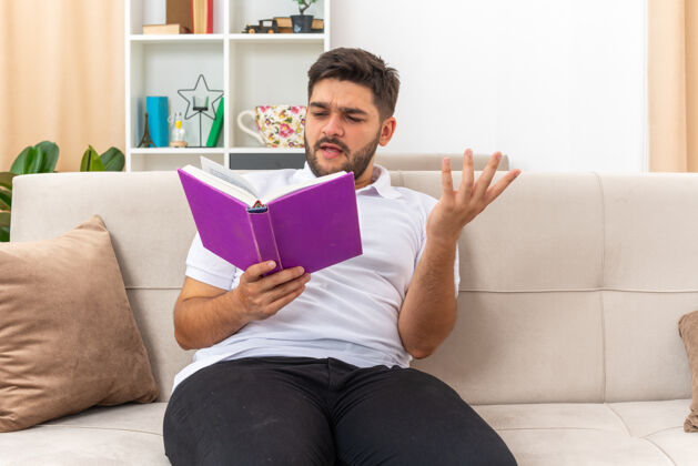 生活一个穿着休闲服的年轻人拿着一本书 表情混乱地坐在客厅的沙发上随意阅读男人