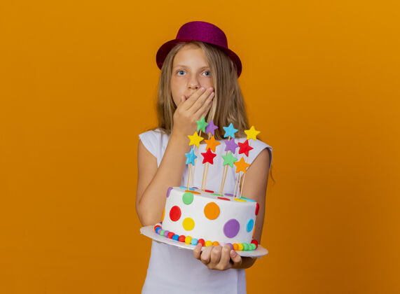 小戴着节日礼帽的漂亮小女孩拿着生日蛋糕大吃一惊 生日派对概念生日站节日