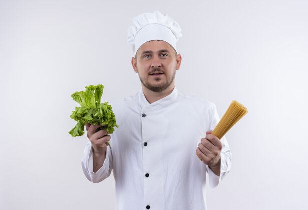 生菜年轻帅气的厨师穿着厨师制服 手里拿着莴苣和意大利面 隔着白墙手持年轻意大利面