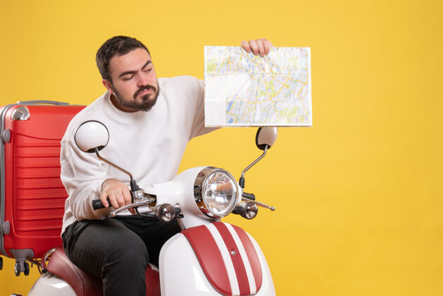 背景顶视图好奇的家伙坐在摩托车上 手提箱上拿着地图孤立的黄色背景摩托车手提箱微笑