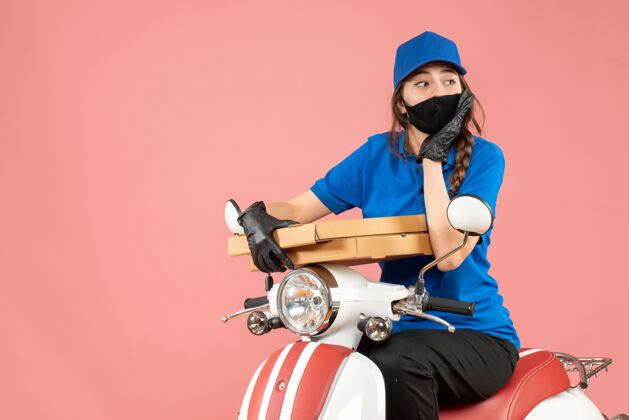 男性戴着医用面罩和手套的女快递员坐在滑板车上 在柔和的桃色背景下传递订单的俯视图设备女信使摩托车