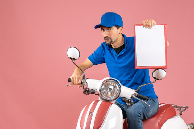 滑板车顶视图自信的信使男子戴着帽子坐在滑板车上显示文件粉彩桃背景快递员显示扩音器
