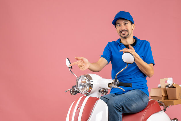 高尔夫前视图的快乐送货员戴着帽子坐在粉彩桃色背景的踏板车上坐着微笑滑板车