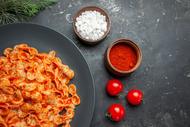 一餐在一个黑色的盘子里放上半张简单的意大利面 在深色的背景上放上不同的香料和西红柿黑胡椒一半