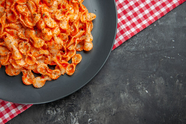厨具半张美味的意大利面 放在一个黑色盘子里 在一条红色的毛巾上 背景是黑色的饭胡椒食物