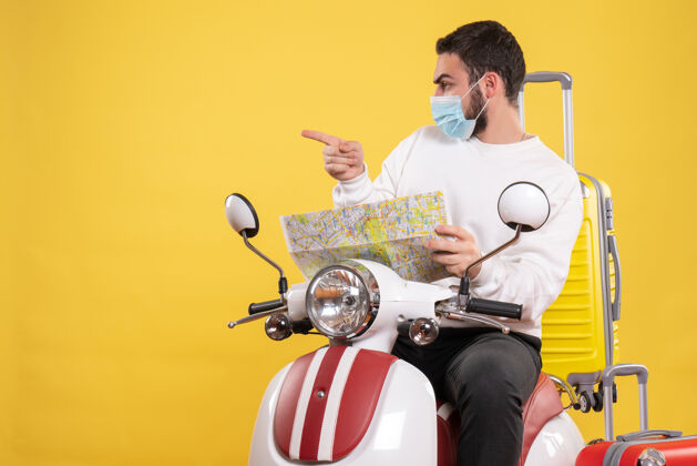 人带着医用面罩的好奇的家伙坐在摩托车上 带着黄色的手提箱 在黄色的地图上展示旅行概念坐着手提箱黄色
