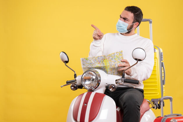 抱着旅行概念的俯视图 戴着医用面罩的好奇的家伙坐在摩托车上 黄色手提箱放在上面 手里拿着地图人黄色医疗