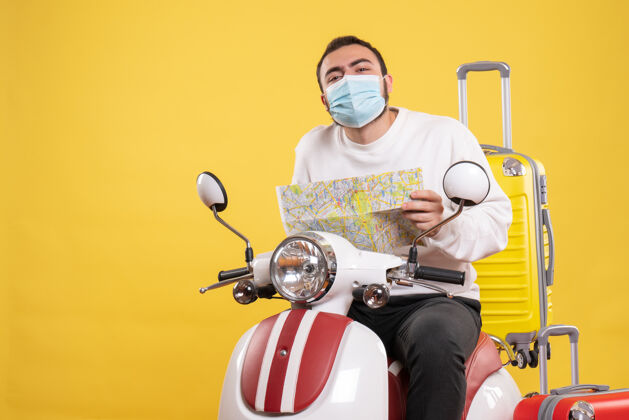 人带着医用面罩的好奇的家伙坐在摩托车上 带着黄色的手提箱 拿着黄色的地图抱着运动医疗