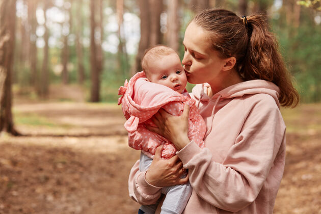 家庭可爱的年轻母亲抱着小女婴亲吻她的户外镜头婴儿夹克孩子