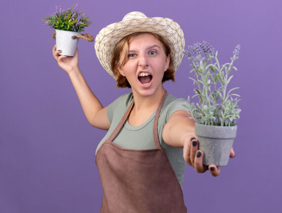 举行恼怒的年轻斯拉夫女园丁戴着园艺帽 手里拿着花盆里的花花园帽子花