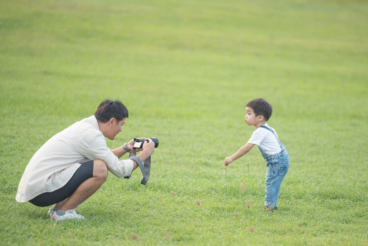 孩子父亲用数码摄像机给儿子录下了快乐的父亲和儿子在公园里的画像微笑学习肖像
