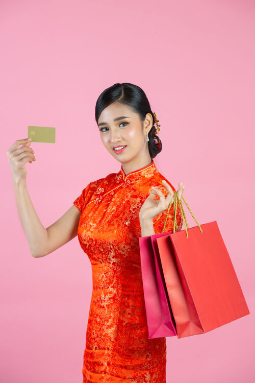年美丽的亚洲女人快乐的微笑和购物在中国新年的粉红色背景女人展示红色