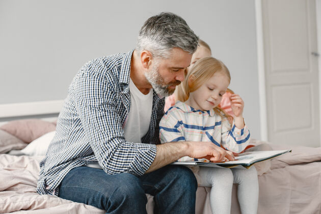 教育为人父母可爱的女孩和爷爷坐在卧室里一起看书年轻人退休老人