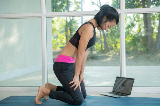 生活练习瑜伽 做向上腹部锁定运动 uddiyanabandha姿势 锻炼 穿着运动服 在笔记本电脑上看健身视频教程 在家坐着锻炼普拉提运动健身