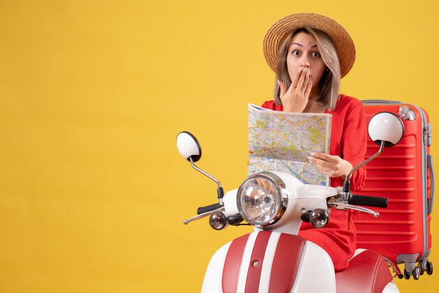 剪影戴着巴拿马帽的漂亮女孩 骑着轻便摩托车 带着红色手提箱 手里拿着地图地图红色帽子