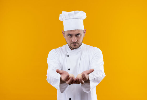 空旷自信的年轻帅哥厨师身着厨师制服 在橙色的墙上伸出空手年轻厨师舒展