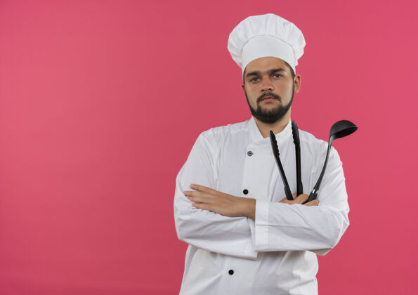 自信自信的年轻男性厨师身着厨师制服 拿着勺子和钳子 隔离在粉红色的墙上 留有复印空间勺子厨师钳子