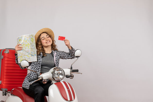 地图骑着轻便摩托车的漂亮年轻女子拿着灰色的卡片和地图摩托车肖像人