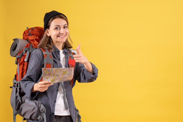 模特微笑的年轻旅行者背着背包拿着地图指着相机衣服长袍女士