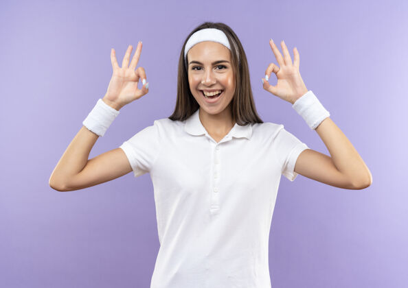 腕带快乐漂亮的运动女孩戴着头带和腕带做ok标志隔离在紫色的墙上头带欢乐穿