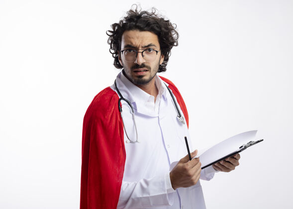 举行严肃的年轻白种人超级英雄戴着眼镜 身穿医生制服 披着红色斗篷 脖子上戴着听诊器 手里拿着铅笔和剪贴板制服剪贴板听诊器