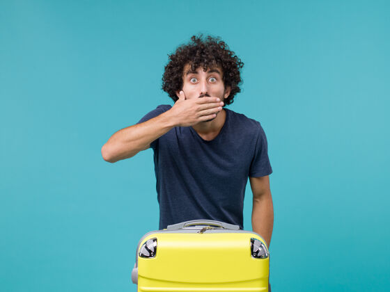 青春带着黄色手提箱和蓝色惊讶表情的度假男人航程蓝色休闲