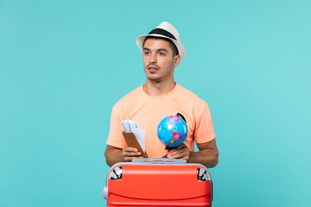 旅行正面图男性在度假时拿着小地球仪和蓝色的门票旅行肖像地球仪