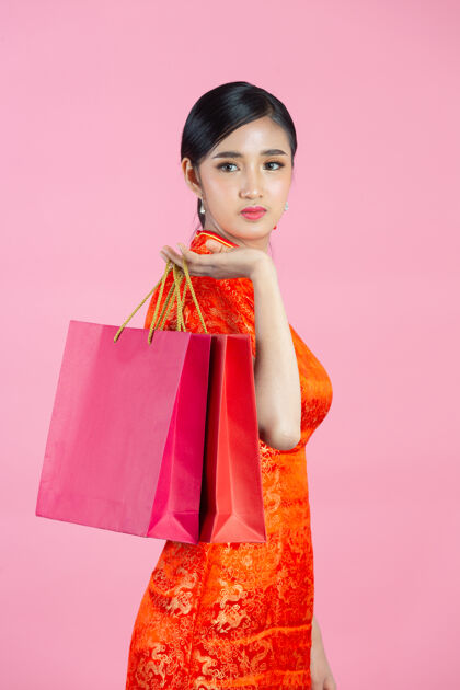 手势美丽的亚洲女人快乐的微笑和购物在中国新年的粉红色背景女人欢呼女孩