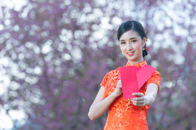 微笑美丽的亚洲女人在中国的新年里展示一些东西和拿红包手势新问候语