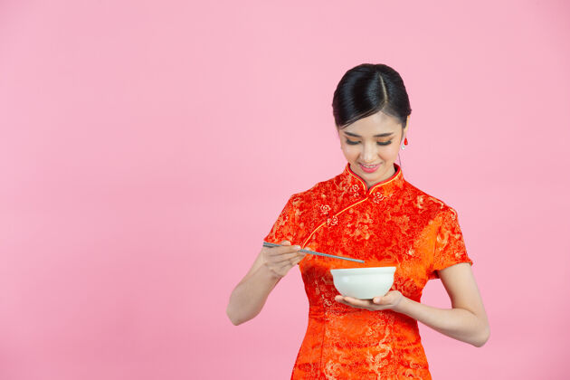 亚洲人美丽的亚洲女人快乐的微笑和吃在粉红色背景的中国新年东方人手势空白