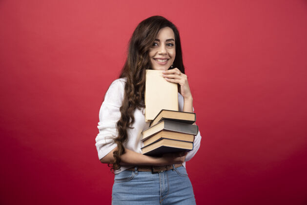 休闲年轻女子拿着书 在红色背景上微笑高质量的照片女人女孩学习