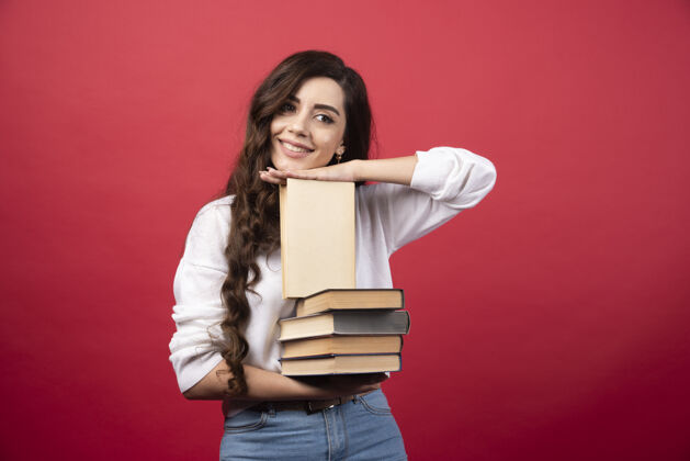 肖像年轻女子拿着书 在红色背景上微笑高质量的照片女性人阅读