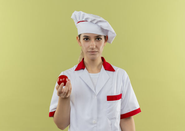 厨师自信的年轻漂亮厨师 身着厨师制服 手里拿着隔离在绿墙上的西红柿年轻烹饪番茄