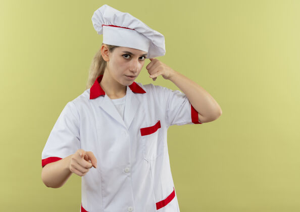 手势令人印象深刻的年轻漂亮厨师在厨师制服做呼叫手势 并指出在绿色墙上与复制空间隔离厨师呼叫印象
