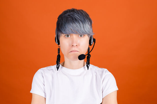 服务呼叫中心助理戴着耳机站在橙色的墙上 脸上带着严重的不开心表情对着镜头站着快乐电话营销