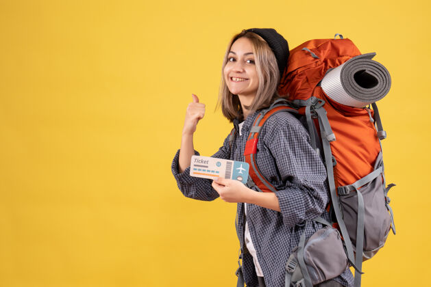 时尚微笑的旅行妇女背着背包拿着车票 手指在后面黑发指向模型