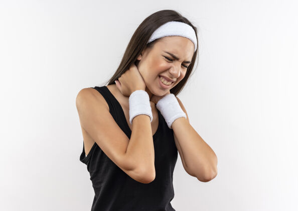 手戴着头带和腕带的疼痛漂亮的运动女孩把双手放在脖子上闭着眼睛隔离在白色的墙上腕带漂亮脖子
