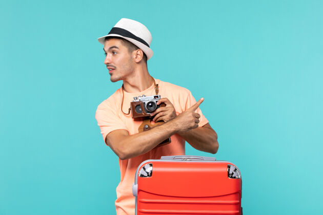 红色带着他的大红色手提箱和相机在蓝色的天空上拍照的度假男人采取旅行蓝色