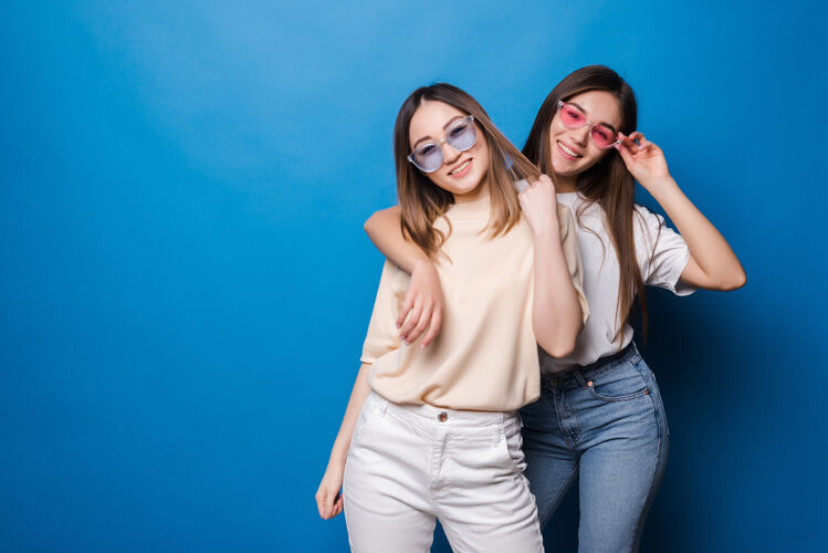 肖像永远的朋友两个戴着太阳镜的可爱女孩在蓝色的墙上微笑着摆姿势微笑乐趣家庭