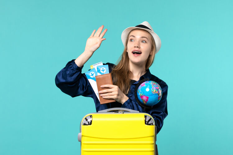 举行正面图年轻女子拿着机票和地球仪在蓝色背景的飞机上海上度假旅行年轻女子肖像地球仪