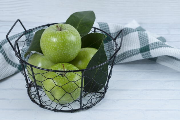 多汁绿色的苹果和叶子放在金属黑色的篮子里 放在白色的背景上高质量的照片有机健康餐桌