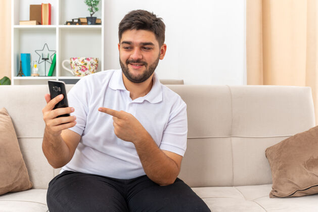 房间一个穿着休闲服的年轻人拿着智能手机 用食指指着它 自信地微笑着坐在客厅的沙发上目录手指手机