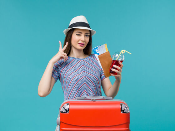 成人前景度假中的女人拿着果汁和浅蓝色背景上的机票远航旅程中的女性海上避暑飞机肖像航行美丽