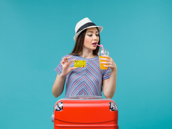 肖像前景：度假的女人拿着果汁和黄银行卡在蓝色的地板上海上旅行举行旅行人